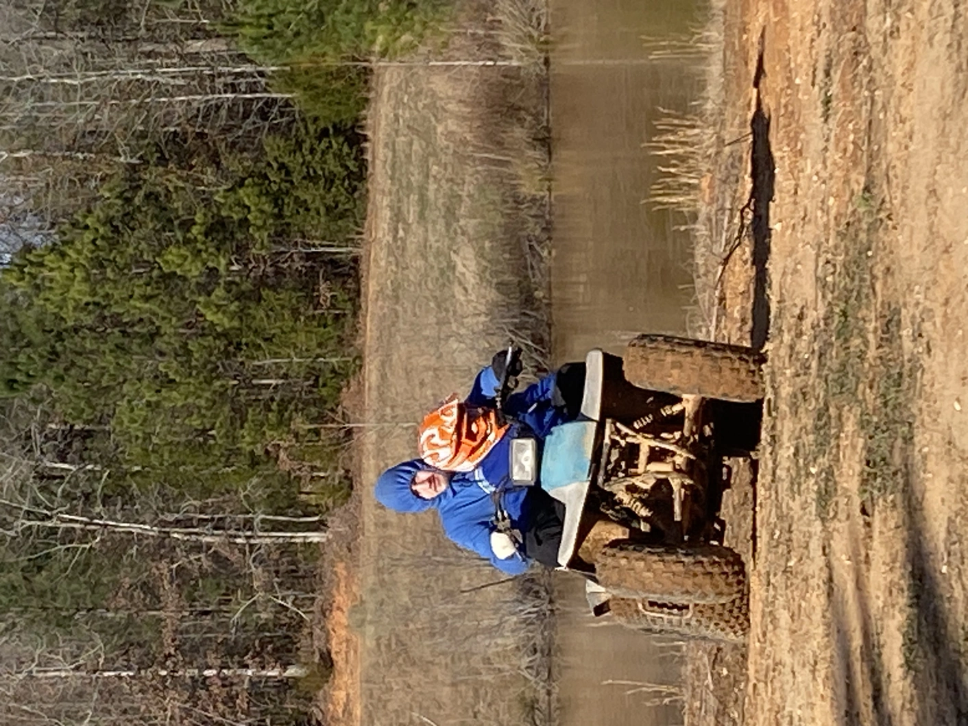 Two people riding an ATV next to a pond, one is an adult, one is a toddler.