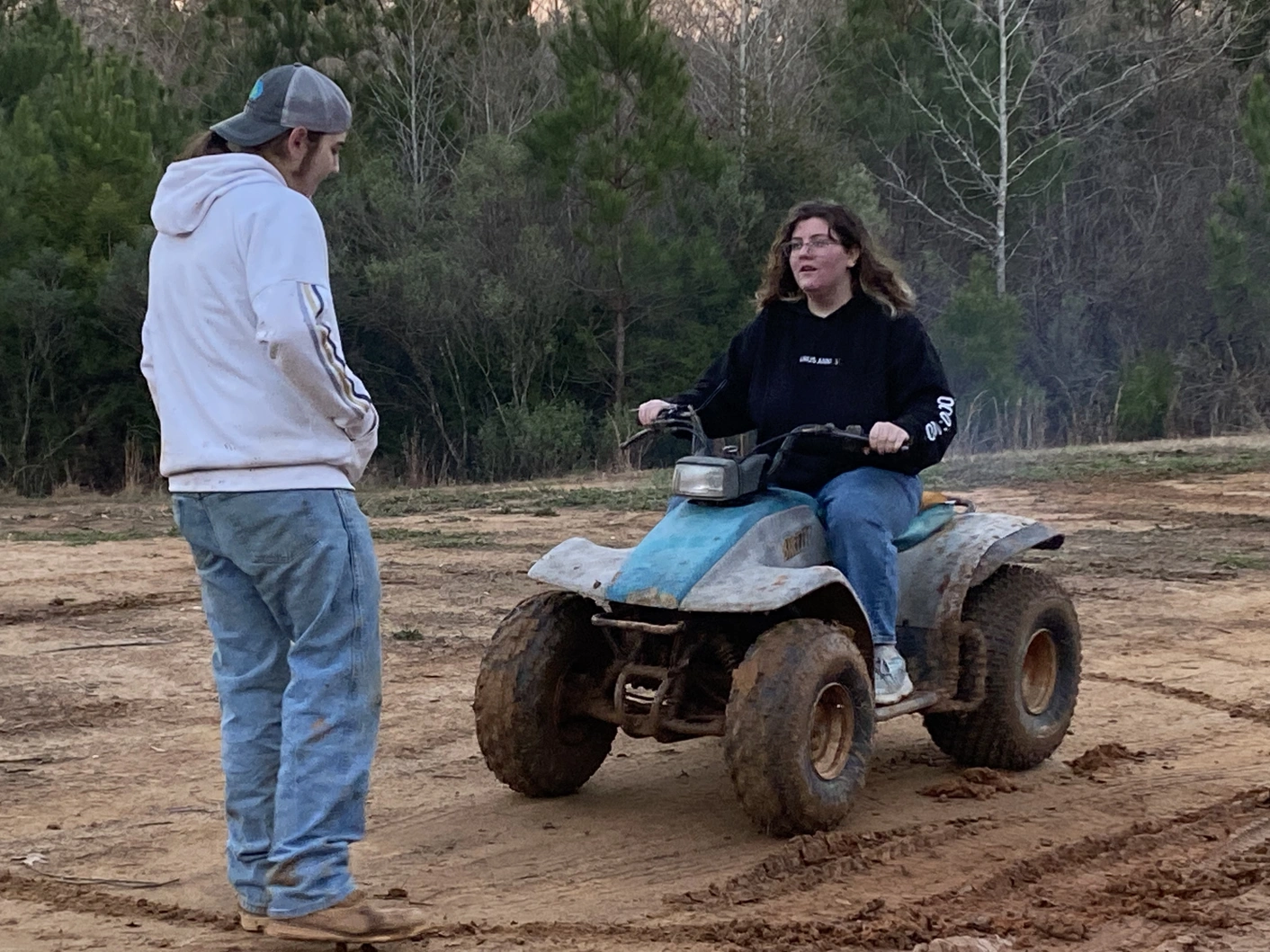 One person sitting on an ATV, and one person standing in front of the ATV