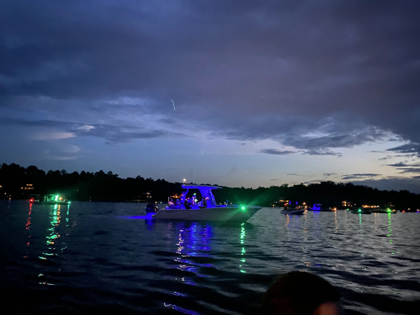 Several boats on a lake at twilight, green and blue lights reflecting on the water