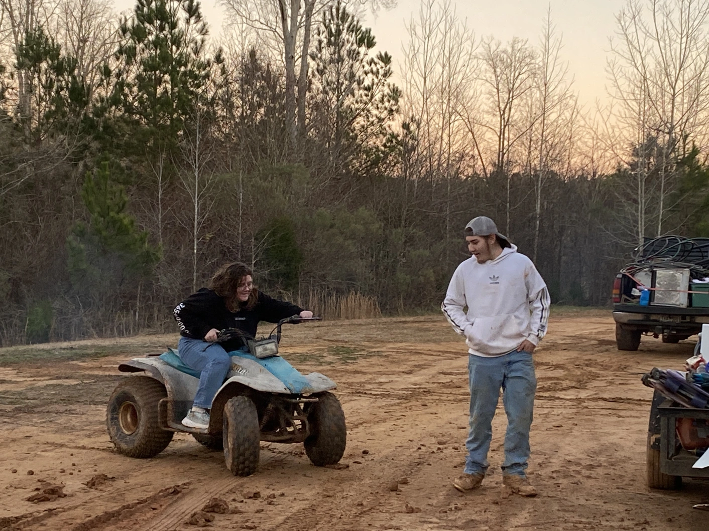 Two people on a dirt road, one riding an ATV