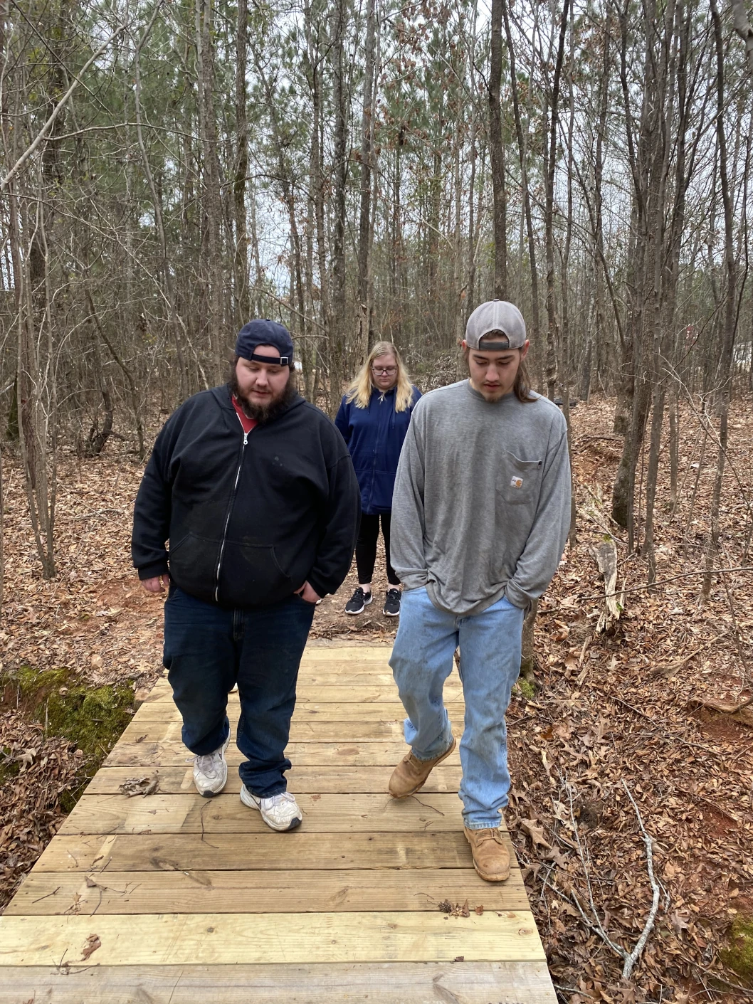 Three people walking across a foot bridge over a creek in the woods