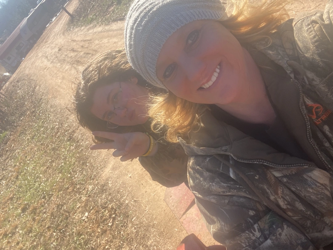 Two people posing in front of camera on a tractor, one throwing a peace sign